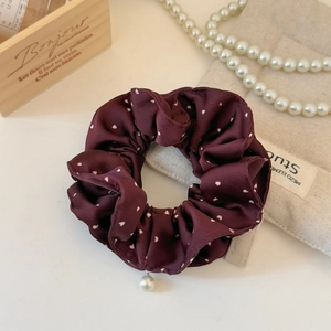 Close-up of a burgundy satin scrunchie with white heart patterns and a pearl pendant