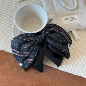 Detail of a large black bow hair clip with pink embroidery and white faux pearls