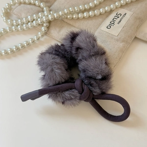 Détail d'un chouchou en peluche grise avec nœud décoratif sur fond de tissu beige doux