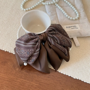 Detailed shot of vintage brown paisley bow hair claw clip with white pearls by a coffee cup