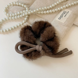 Détail d'un chouchou en fausse fourrure marron avec nœud sur fond beige élégant