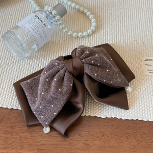 Détail d'une pince à cheveux avec nœud en tricot marron, pois blancs et perle fine