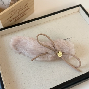 Detail of plush bow hair clip with faux fur texture and a round golden logo charm