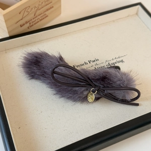 Close-up of plush bow hair clip with leather cord and gold embossed metal pendant