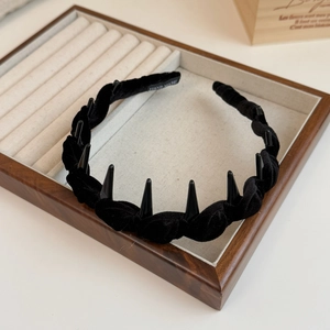 Handmade black velvet twisted headband with punk spikes on a wooden jewelry display
