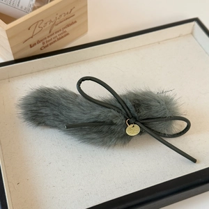 Detailed macro view of dark grey plush bow hair clip with gold metal emblem and leather trim