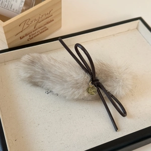 Macro shot of fluffy beige faux fur hair clip with brown leather bow and gold charm