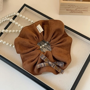 Détail d'un chouchou à carreaux marron avec nœud et étiquette Hand Made sur un plateau