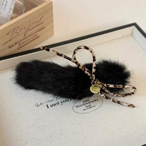 Close-up of black faux fur hair clip with leopard bow and gold pendant detail
