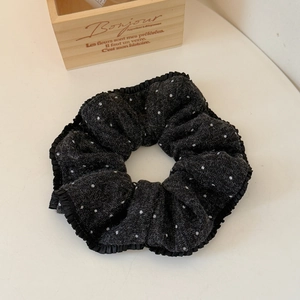 Detail of black polka dot knitted scrunchie with ruffled pleats on a minimal background