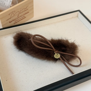 Detail of dark brown plush hair clip with bow and gold metal tag on beige tray