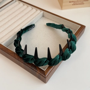 Detail of dark green velvet braided headband with black punk spikes on wood tray