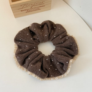 Close-up of a brown knit scrunchie with white polka dots and beige ruffled lace edges