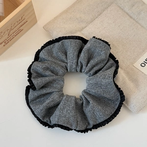 Detail shot of elegant gray knitted scrunchie with delicate black lace trim on a wood tray