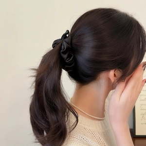 Detailed view of a black satin pleated scrunchie styled on a sleek high ponytail