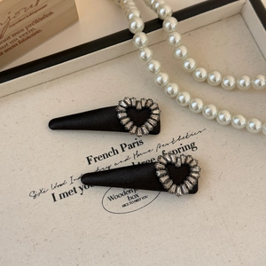 Close-up of black velvet hair clips with rhinestone hearts on white fabric background