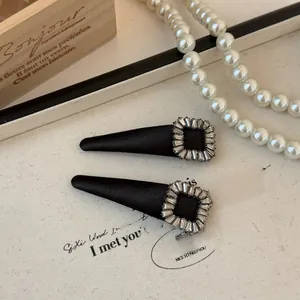 Detailed close-up of a black satin hair clip featuring a sparkling baguette diamond buckle