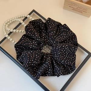 Detail of a black polka dot scrunchie displayed with a pearl necklace in a classic setting
