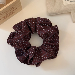 Close-up of a burgundy polka dot fabric scrunchie with white and light blue dots