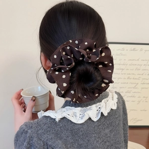 Chouchou satiné marron foncé à pois blancs porté sur un chignon volumineux tendance