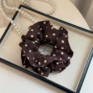 Détail d'un chouchou marron à pois avec tissu plissé sur un plateau à bijoux chic