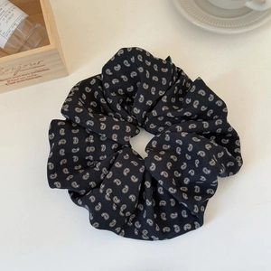 Close-up of black oversized scrunchie with white and gold paisley floral patterns