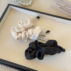 Close-up of pleated satin banana clips in beige and black on an elegant display tray