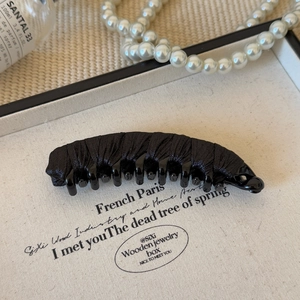 Detailed view of elegant black fabric wrapped banana hair clip on a minimalist display