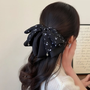 Elegant black satin floral bow hair clip with teardrop beads worn on half-tied hair