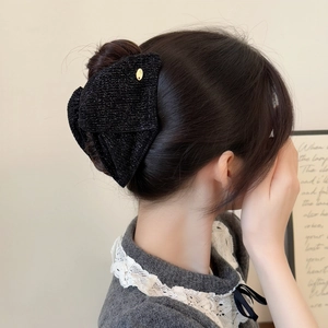 Detail view of a black glitter velvet hair claw with a small gold metal emblem in hair