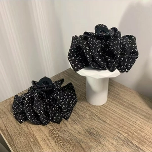 Elegant black and white patterned fabric hair claw clips on white geometric display stand