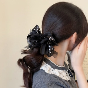 Detail showing the sheer organza fabric texture of a black polka dot bow hair scrunchie