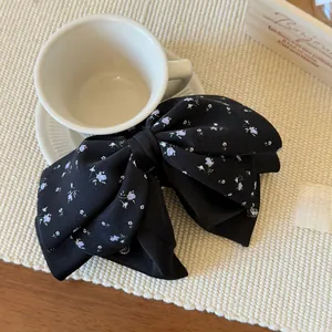 Detail view of a large black floral satin bow hair clip on a minimalist white background