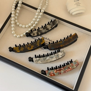 Detail view of five acetate banana hair clips with marble patterns in an elegant tray