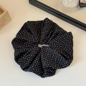 Detail view of a black floral fabric scrunchie on a minimalist beige background