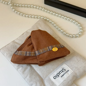 Détail d'une pince à cheveux en tricot marron avec logo cerise et ruban à carreaux