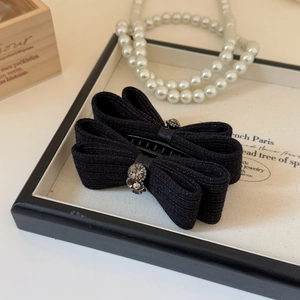 Close-up of elegant black knitted bow hair clip with sparkling rhinestone flower and plastic claw