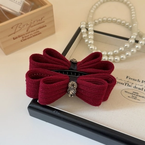 Close-up of wine red ribbon bow hair clip with sparkling rhinestone flower and texture