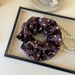 Detailed view of dark purple polka dot silk scrunchie on an elegant tray with pearls