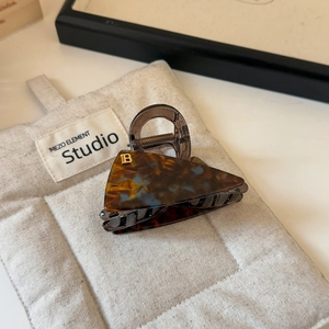 Detail of tortoise shell acetate hair claw clip with gold B logo and blue accents