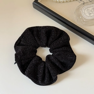 Close-up of black knitted hair scrunchie with silver glitter details and pleated texture