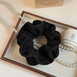 Detailed view of black sparkling scrunchie with silver threads on a luxury display tray