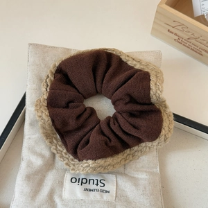 Detailed close-up of dark brown knit scrunchie with beige crochet lace edges on fabric