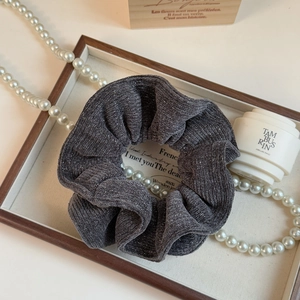 Detail shot of a dark grey knit scrunchie with sparkling silver yarn on a wooden tray