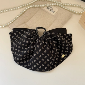 Detail of black paisley fabric shark hair clip with elegant ruffles and gold label