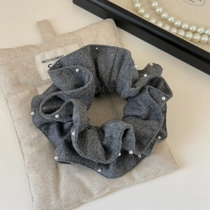 Detail of grey knitted hair scrunchie with white pearls on a branded beige fabric pouch