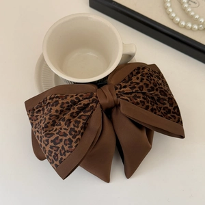 Close-up of leopard print satin bow hair clip with black claw on a cozy table setup
