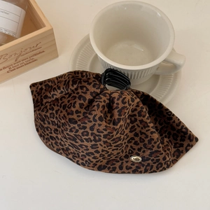 Detailed view of leopard print fabric hair claw with a small golden Wings metal tag