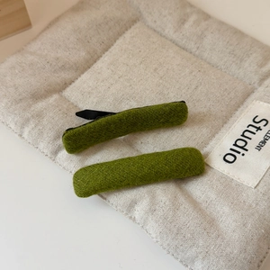 Detail of green wool fabric hair clips on beige linen background with studio props