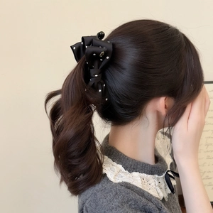 Close-up of a black silk bow hair clip with white polka dots worn on a low ponytail